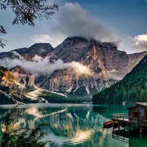 Mountain lake with cabin and clouds over rocky peaks