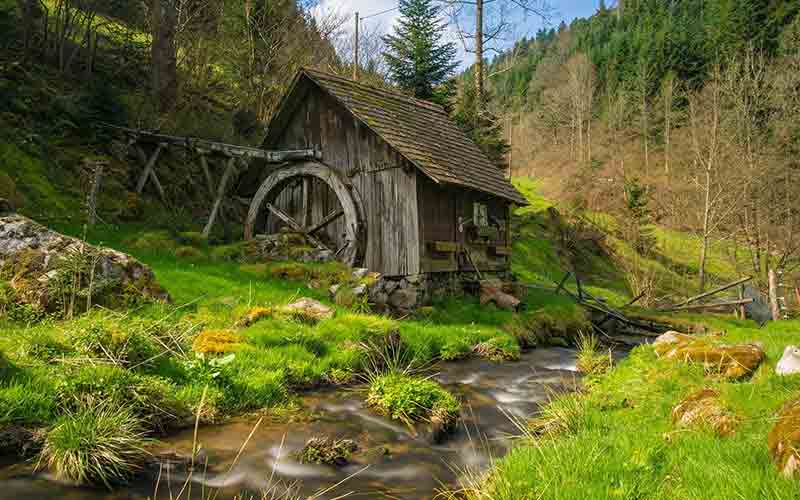 Old wooden watermill beside a bright stream in a green valley